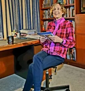 Winifred Hughes smiles while sitting at her desk, holding a magazine that reads: See beautiful birds every day